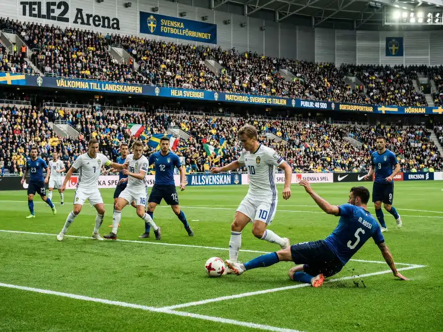 Fotbollsspelare i vita tröjor under en intensiv match med fullsatt läktare i bakgrunden