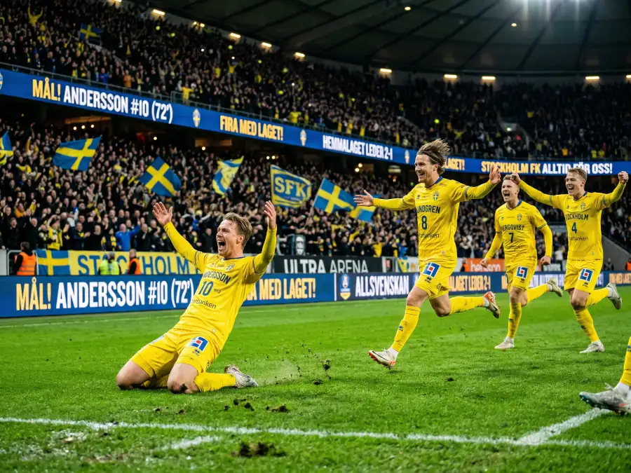 Fotbollsspelare i gula tröjor firar ett mål under en kvällsmatch på en stor arena